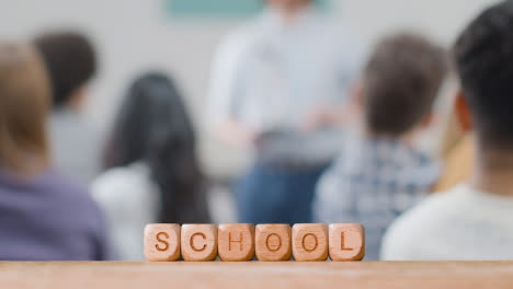 Education-Concept-With-Wooden-Letter-Cubes-Or-Dice-Spelling-School-With-Student-Lecture-In-Background